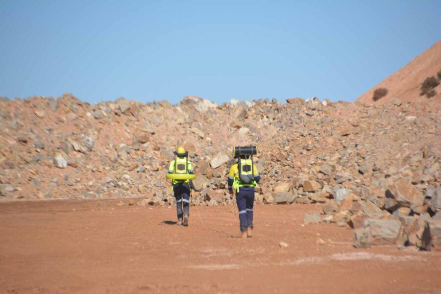 Two operators in hi-vis towing the Loupe TEM system across a red-dirt mine bench